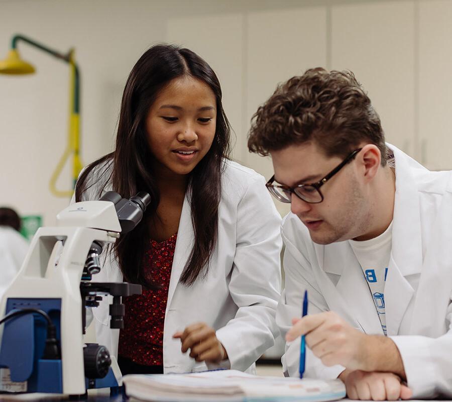 two biology students in a laboratory looking at a specimen in a microscope